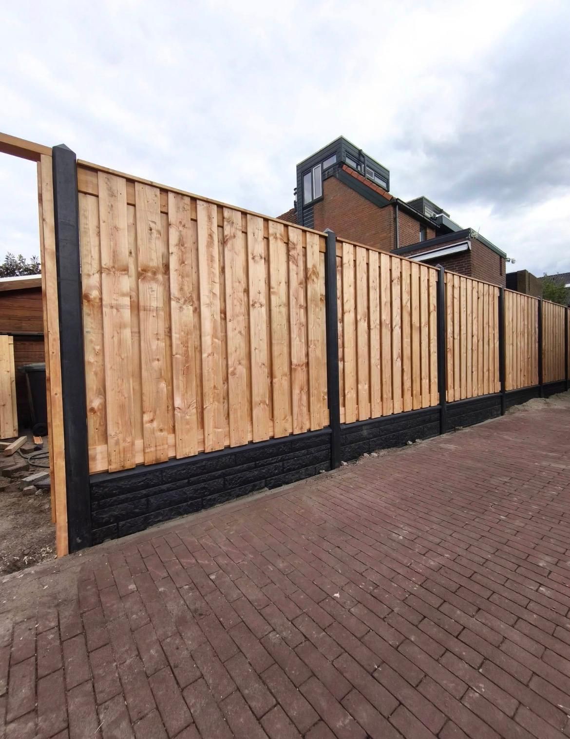 Nieuwe schutting in grenenhout op een zwarte onderplaat, met border