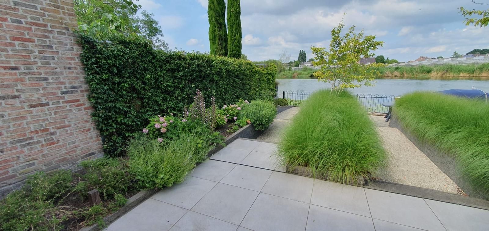 Aangelegde tuin aan het water met terras, siergrassen en border